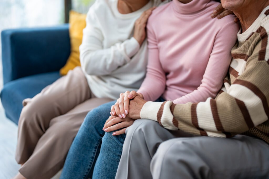 Drei Personen sitzen gemeinsam auf einem Sofa in Herne und halten sich unterstützend an den Händen